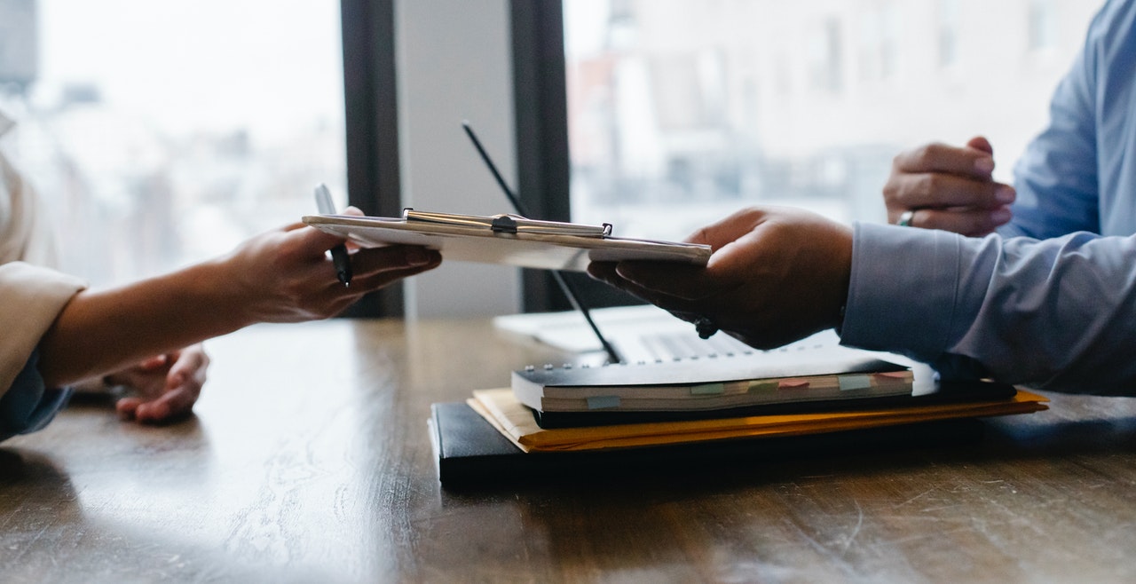 dos personas pasándose papeles de trabajo